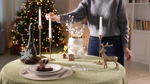 Woman lighting up candles at table with Christmas decor and stylish setting indoors, closeup