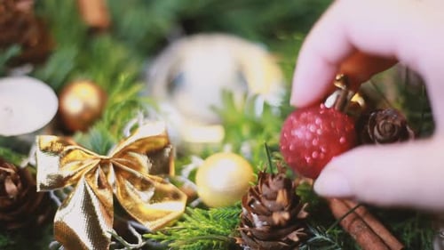 Hand Places Red Ornament on Christmas Wreath