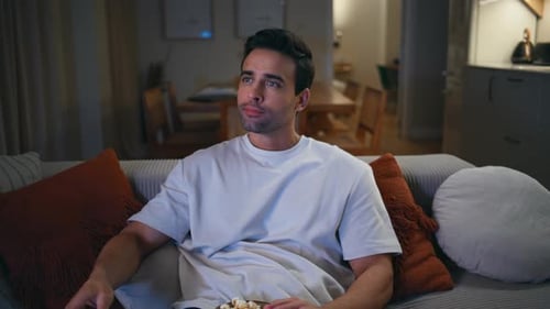 Man Relaxes on Couch Watching Television and Eating Popcorn