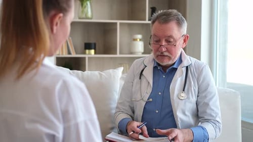 Senior Man Doctor Examining Yound Woman in Doctor Office or at Home Girl Patient and Doctor Have