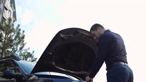 Junger Mann vor dem Auto, Geschäftsmann steht vor der geöffneten Motorhaube und hält einen Schraubenschlüssel in der Hand, um das Auto zu reparieren