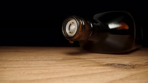 Hand Tilts Dark Glass Bottle and Liquid Drips