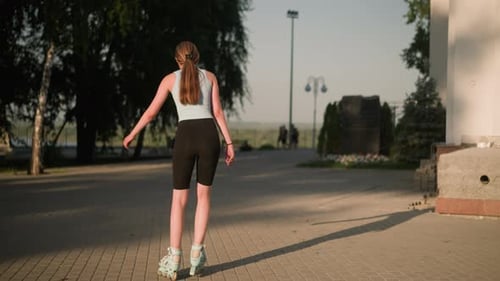 Back View of Young Lady Skating Outdoors on Sunny Day Near Building and Trees