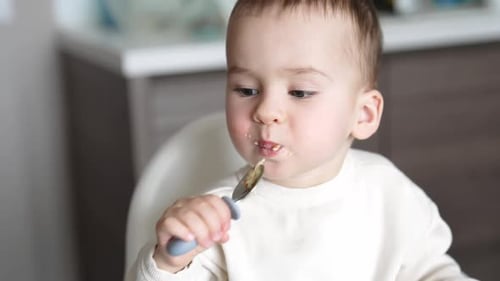 Baby eating food with a spoon at home