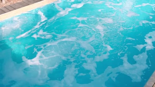 Blue water in a pool bubbles with the hydro massage system turned on, creating foam and bubbles on t