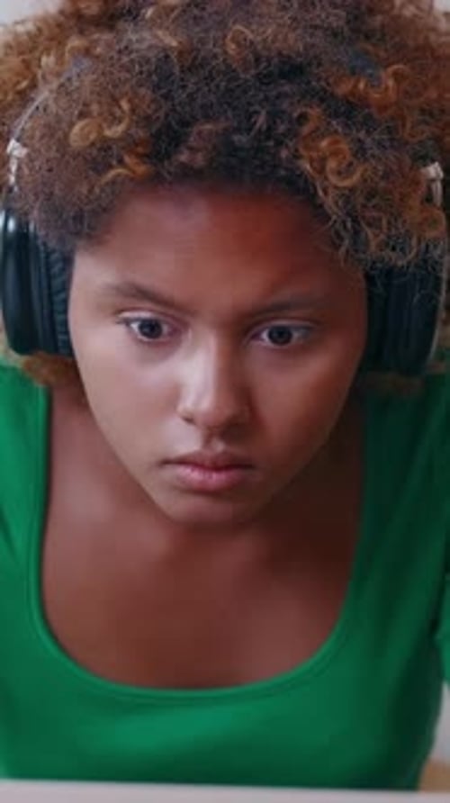 Young Woman Wearing Headphones Shows Frustration While Looking at Laptop Screen