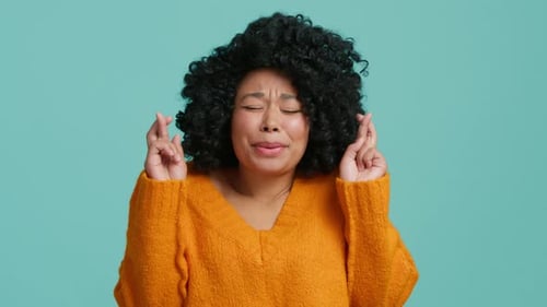 Hopeful Woman with Crossed Fingers on Blue Background