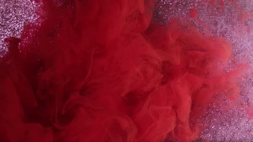 Vibrant Red Ink Swirling in Glittery Water