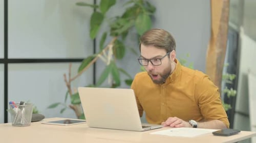 Young Man Celebrating Online Success on Laptop in Office