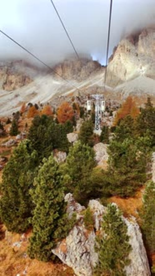 Aerial View of Cable Car Over Autumn Forest in Dolomites with Mountain Peaks in Clouds