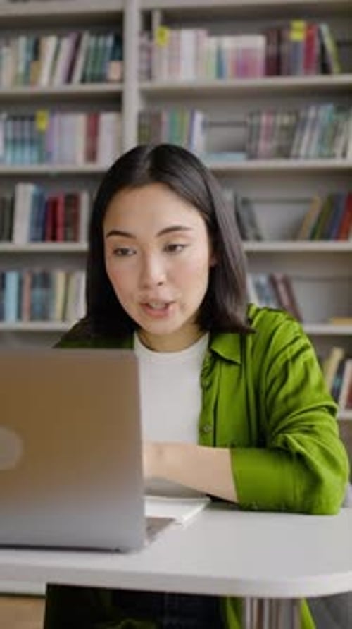 Smiling woman in library talking on laptop