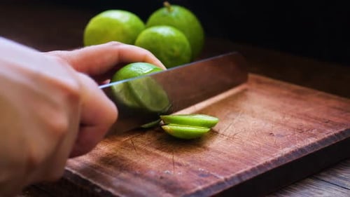 Hands Slicing Lime on a Wooden Cutting Board