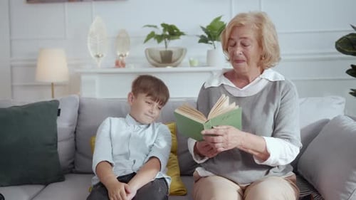 Grandmother Reading Book with Grandson, Giving Him Phone
