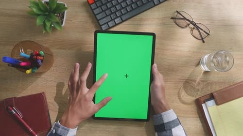 Top down view of man's hands using a mock up green screen tablet on a desk