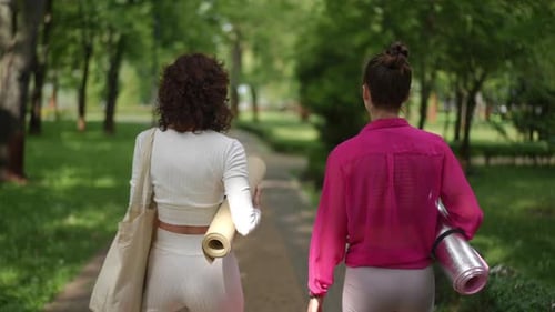 Two Women Walking in the Park Carrying Yoga Mats in Stylish Activewear