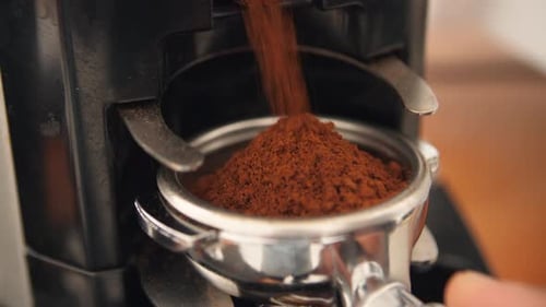 Close up on coffee grinder dispensing coffee ground into portafilter in coffee shop