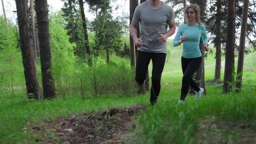 Sportive young people running. Couple work out and run up the hill in the park during the day