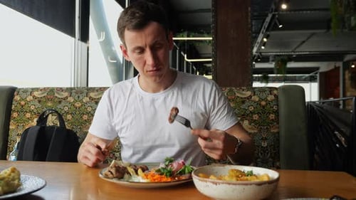 Man Eating Meat and Vegetables in Restaurant