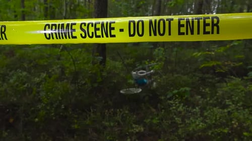 Police line crime scene tape in front of a childs bicycle in a dense and eerie forest during autumn.