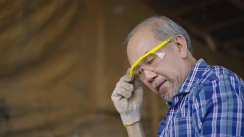 An elderly carpenter inspecting a wooden plank in a workshop before beginning his furniture project