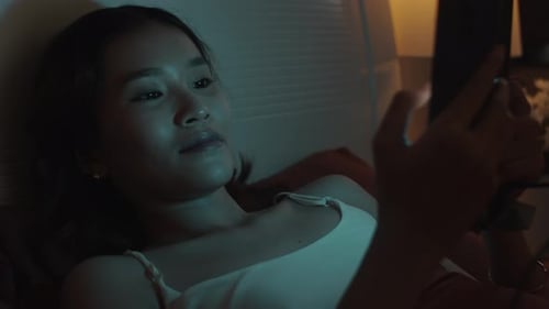 Young Woman Scrolling Social Media in Bed before Sleep at Late Time