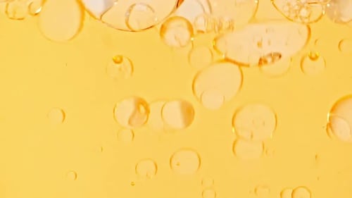 Zeitlupe sich bewegender gelbgoldener Ölluftblasen im Wasser, die auf hellweißem Hintergrund aufsteigen