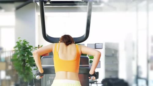 Back view of motivated fit lady in sportswear pulling on bar, doing pull-ups practicing biceps muscl