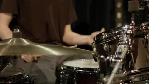 Close up of a professional drummers arms, playing on a drum kit and practicing on stage with a dark
