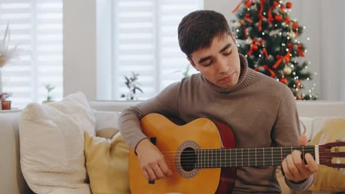 Man plays guitar on couch at Christmas time
