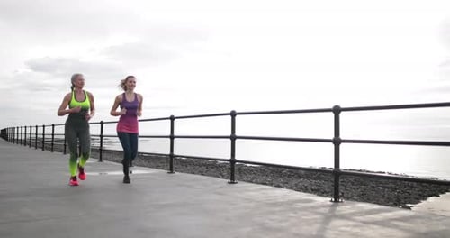 Two Women Jogging Along the Coastline Boardwalk