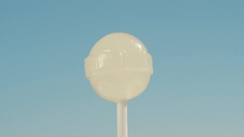 A round white lollipop on a stick, spinning against a blue sky background. Close-up.