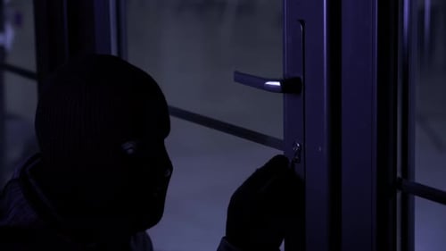 Gefährlicher Mann mit Sturmhaube in Handschuhen mit Picklocks versucht, das Schloss zu knacken und die Tür zum Zimmer zu öffnen