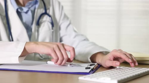 Woman Doctor Typing and Writing at Desk