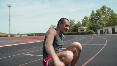 Athlete Stretching on Running Track on Sunny Day