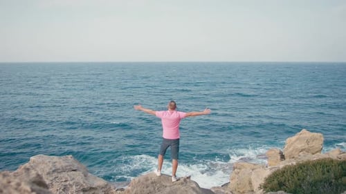 A Tourist Stands on a Rocky Cliff with His Arms Spread Wide