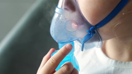 Close Up View of Little Girl are Sitting and Holding a Nebulizer Mask Leaning Against the Face