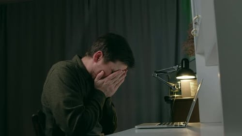 Distressed Man Types on Laptop in Dark Room