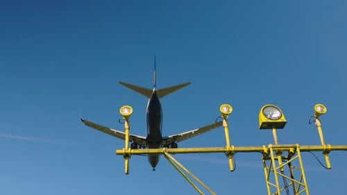 Airplane gliding through the clear blue sky over airport runway lights