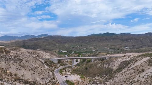 Flight reverses from a pristine newly constructed rail bridge revealing a road below and a vast rugg