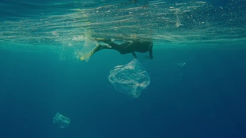 Frau in Schnorchelausrüstung sammelt Plastikmüll auf, der im türkisfarbenen Wasser schwimmt
