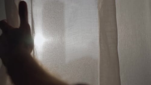 Hands open the curtain on the window. Sun rays shine through. Urban city in the background view.