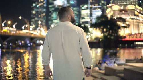 Young man admiring Singapore city lights reflecting on the riverside at night