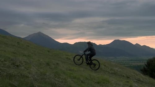 Young athletic man on MTB e-bike pedalling up the hill in the morning. Sun is waking up.