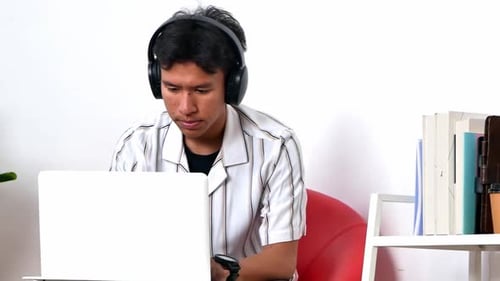 Focused young man concentrating on laptop screen wearing headphones working from home office