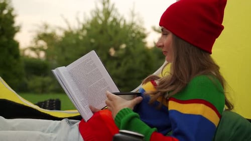 Woman in a Red Hat Lying Down Reading a Book Outdoors in a Tourist Tent in a National Park