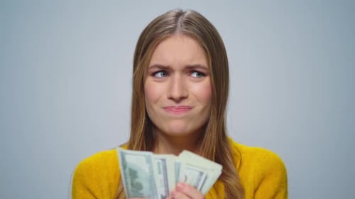 Woman Holding Money with Concerned Expression on Grey Background
