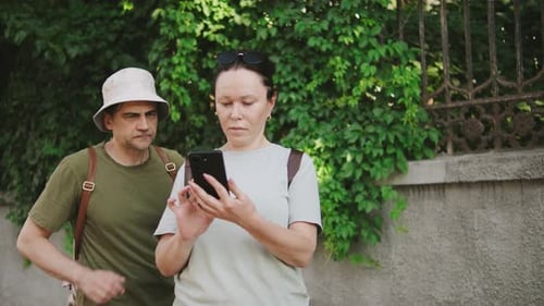 Touristin geht im Freien spazieren, während sie mit einem Mann in Freizeitkleidung in der Nähe im Grünen telefoniert