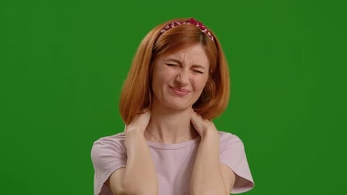Young red haired woman with neck pain over isolated green screen background.