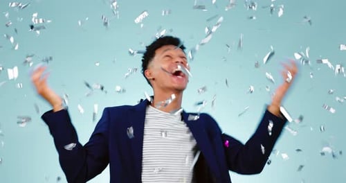 Confetti, dance and celebration of excited man in studio isolated on a blue background