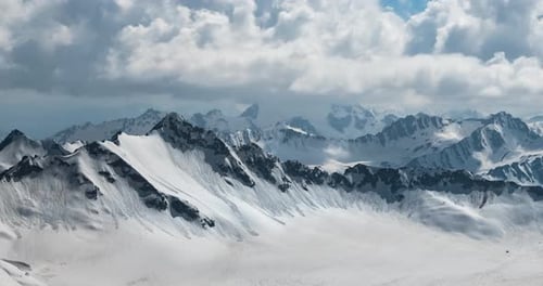 Air flight through mountain clouds over beautiful snow-capped peaks of mountains and glaciers.